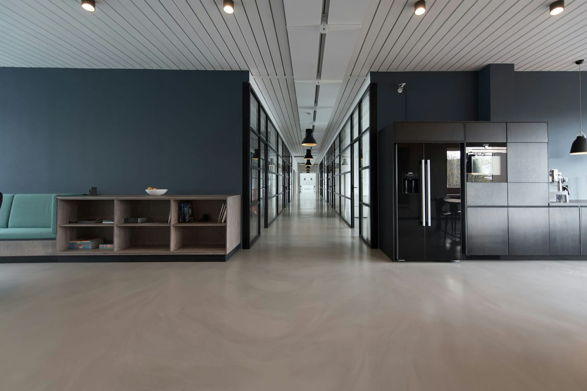 An empty, sunlit office corridor with glass walls and desks